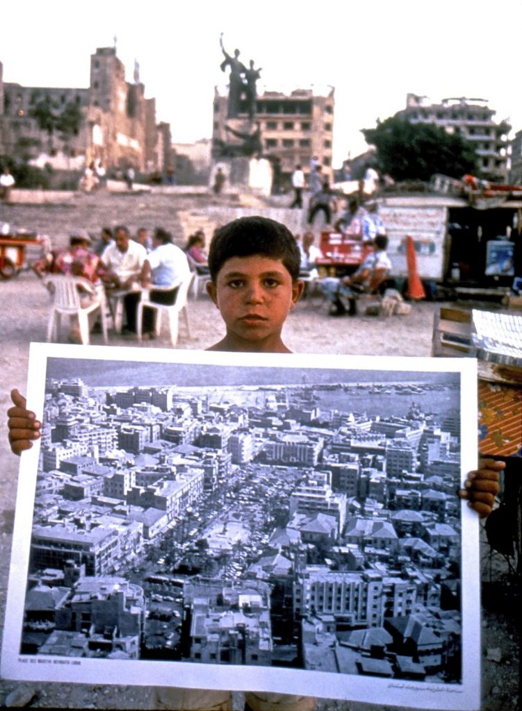 Civil war photograph showing a boy carrying an image of beautiful downtown. In the background, Downtown is in shambles. Beyond what words can tell. Taken by George Azar