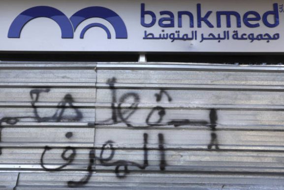 “Down with the rule of the bank” reads this graffiti on the door of Bankmed, one of the top five banks in Lebanon. A default deals a major blow to the banking system in Lebanon. (AP / Financial Times)