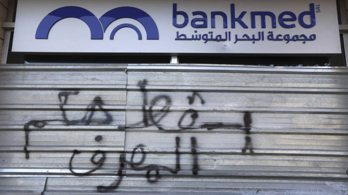 “Down with the rule of the bank” reads this graffiti on the door of Bankmed, one of the top five banks in Lebanon. A default deals a major blow to the banking system in Lebanon. (AP / Financial Times)