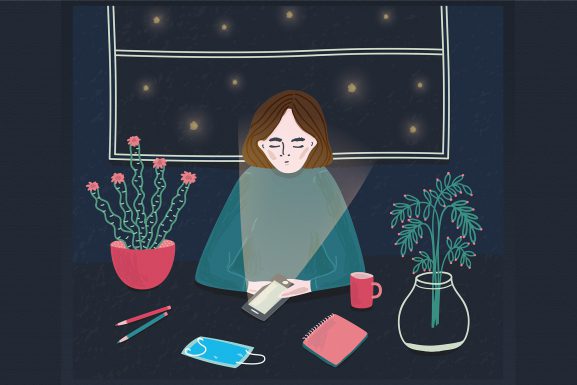 Illustration of woman sitting at a desk and using her phone at night with a facemask in front of her. For Speak Up COVID article