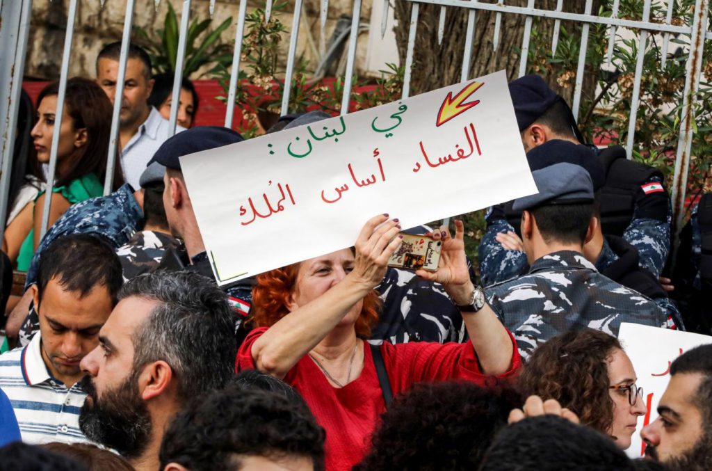 Protester holding up a sign that reads "In Lebanon, corruption is the basis of rule," outside the Justice Palace in Beirut on 6 November (Middle East Eye via AFP)