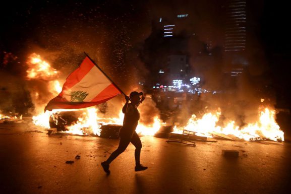 A protester holding the Lebanese flag runs as protesters block the Jounieh Tripoli highway with flaming tires in Beirut late on June 11, 2020. (Photo: CNN)