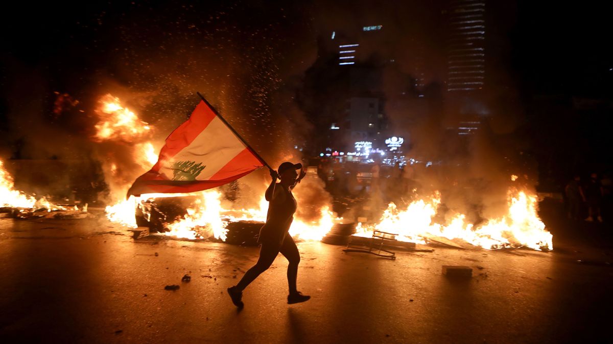 A protester holding the Lebanese flag runs as protesters block the Jounieh Tripoli highway with flaming tires in Beirut late on June 11, 2020. (Photo: CNN)