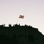 Protesters in Beirut stand on rooftops and wave a Lebanese flag. (Photo: Marylin Chahine) | Protest adapting article