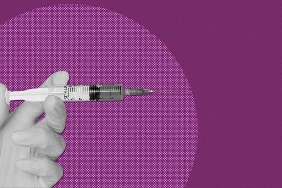 Gloved hand holding a vaccine needle with a purple backgroun