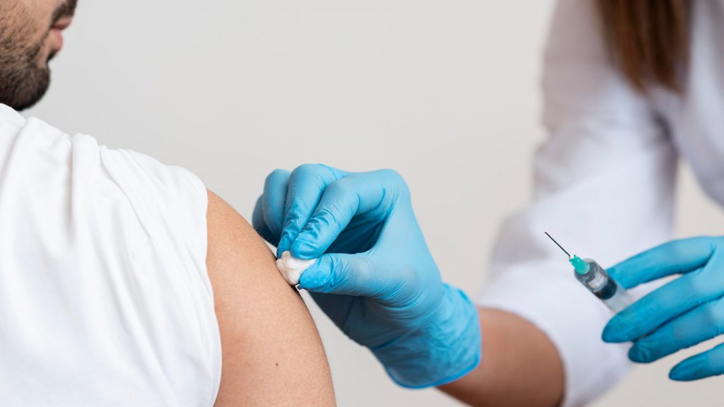 Doctor holding a syringe in one hand and sterilizing shoulder of patient with the other.