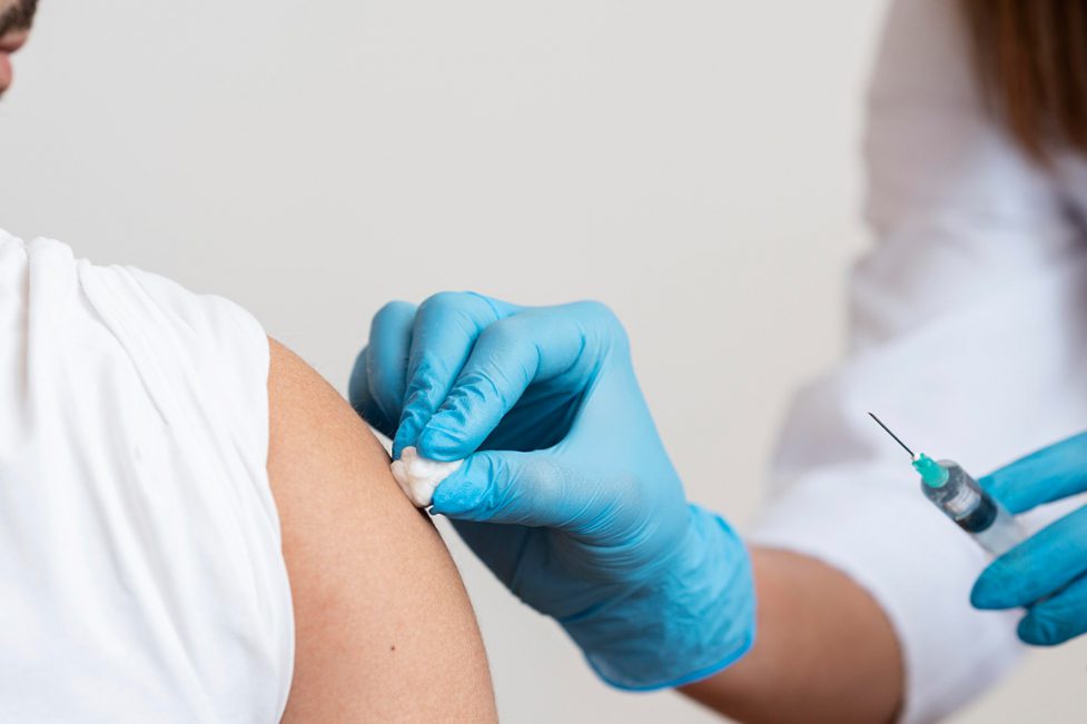 Doctor holding a syringe in one hand and sterilizing shoulder of patient with the other.