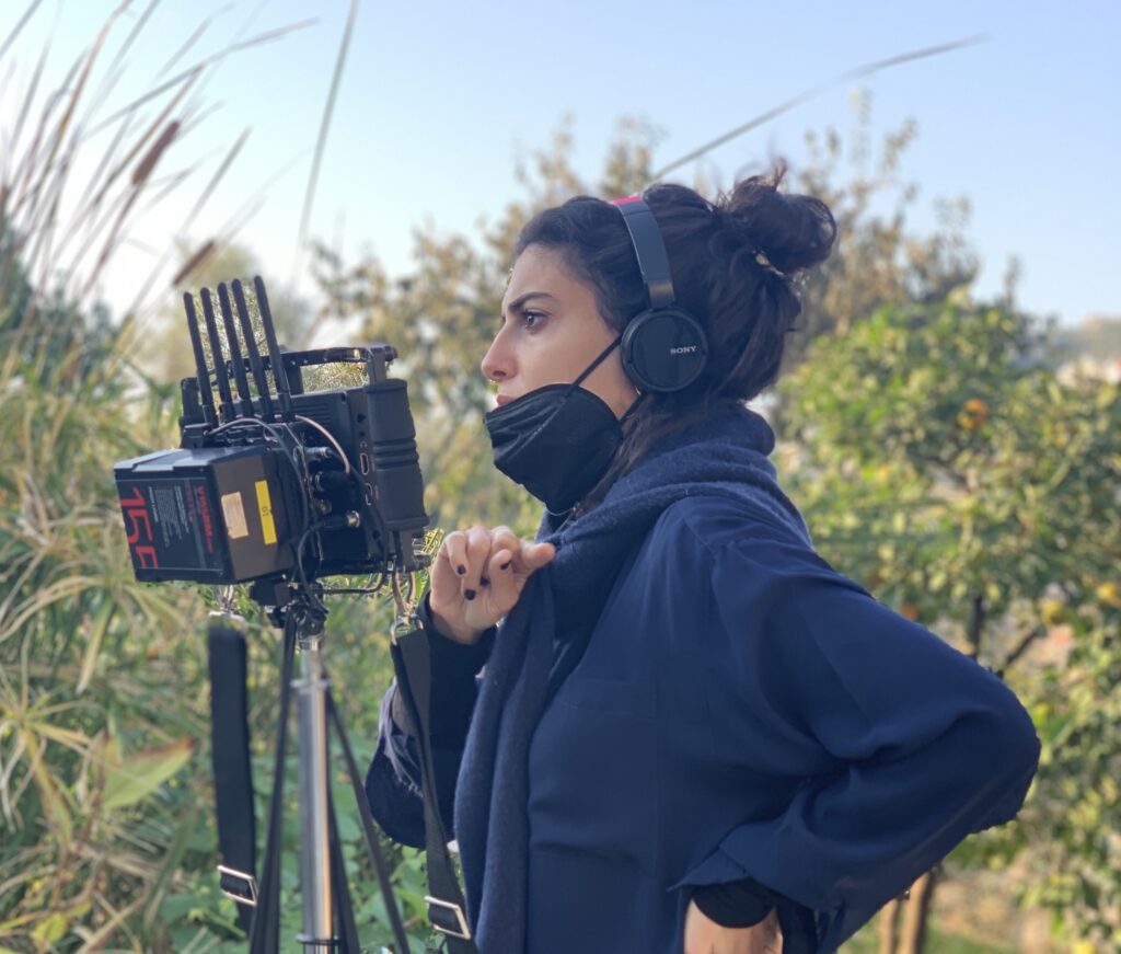 Shot of Mounia Akl on set, wearing a COVID-19 mask and standing behind a camera