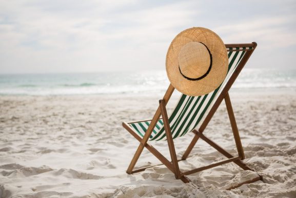Straw hat kept on empty beach chair.
