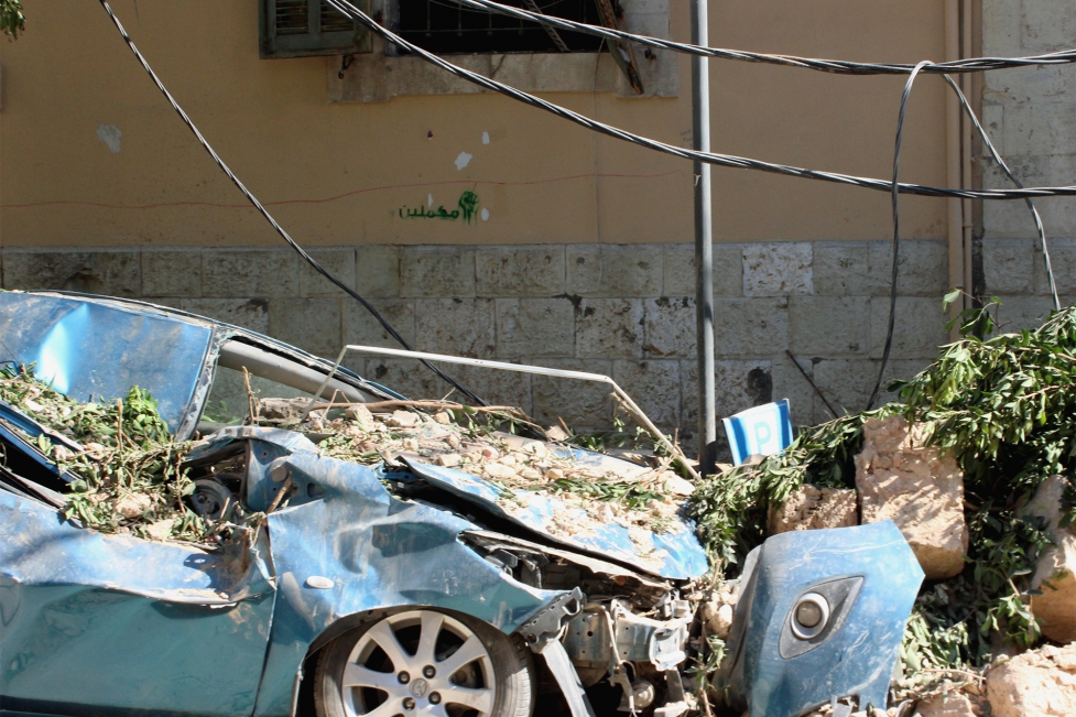 Ablue car is wrecked at the side of the road, covered in debris from a nearby building after the Beirut blast.