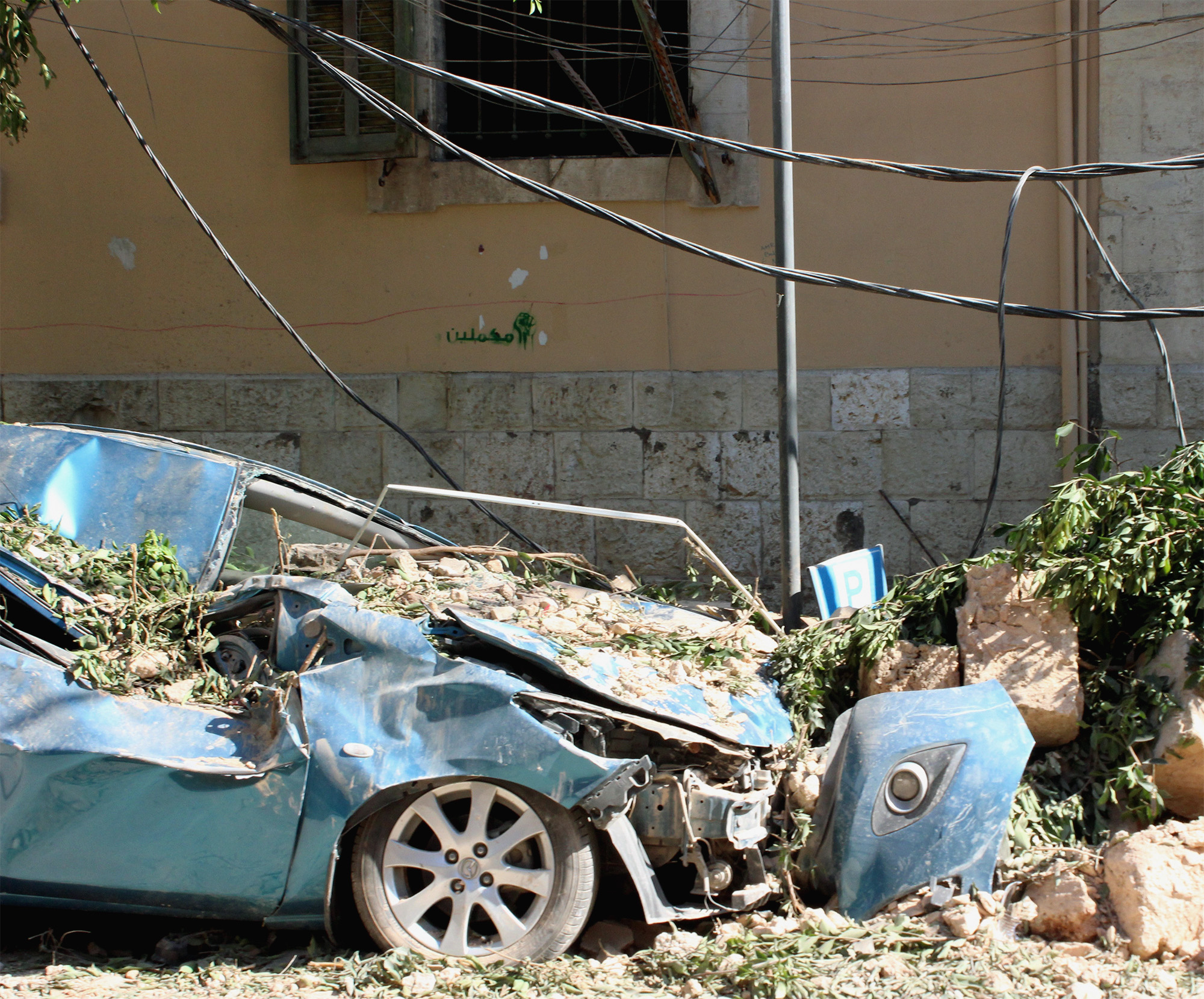 Ablue car is wrecked at the side of the road, covered in debris from a nearby building after the Beirut blast.